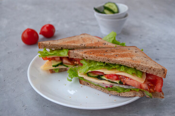 Delicious sandwich with fresh lettuce leaves, tomatoes, cucumbers and cheese on a grey table background.