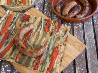 a slice of coca de recapte, a typical Catalan pizza-like savory pie, made with grilled aubergines and red pepper, and pork sausage, on a rustic wooden table