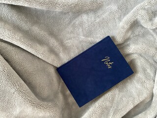 A notebook with a blue velvet cover on a gray terry blanket. The inscription 
