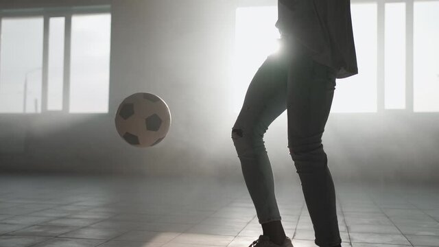 A close-up black man juggles a soccer ball in the sunlight in the garage. Football freestyle at sunset in an urban environment. Dust and sunset
