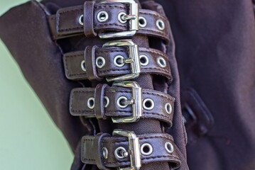 a row of brown leather straps with gray metal buckles on the fabric of the bag