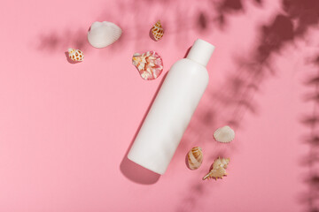 White cosmetic bottle with face cream or lotion and telana against a pink background with seashells...