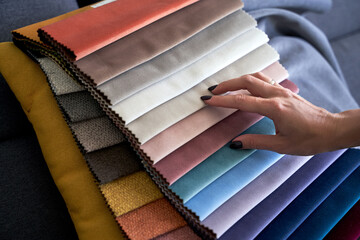 Choosing upholstery fabric color and texture from various colorful samples in a store. Female customer hands touching textile. - obrazy, fototapety, plakaty