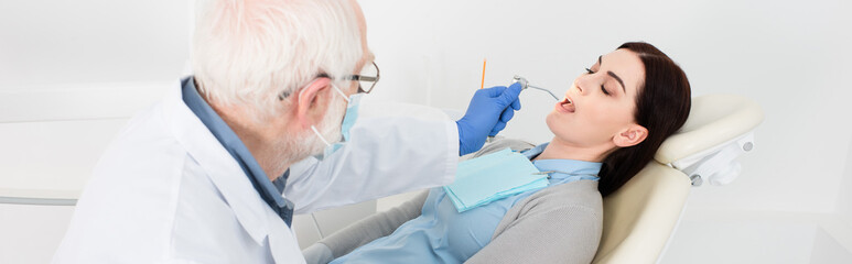 senior dentist in medical mask making teeth treatment of attractive woman in dental chair, banner.