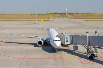 White commercial airplane docked on apron outside airport terminal with passenger boarding bridge....