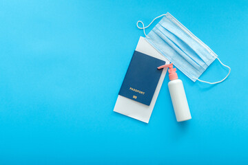 Protective medical mask sanitizer and passport airplane ticket. Concept vacation safe travel flights during covid and coronavirus lockdown. Flat lay on color blue background with copy space. 