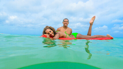 Fototapeta na wymiar Couple at the beach playing, in the water with a float, interracial, black