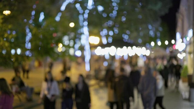 Crowded street of the big evening city. Defocused shot of people walk along the street with evening illumination, visit cafes and restaurants