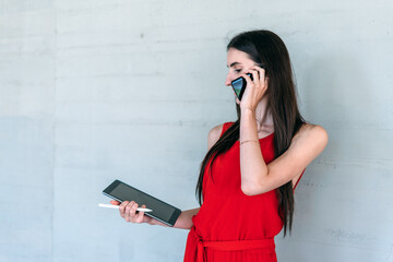 Young business woman holding a tablet while calling with her cell phone.
