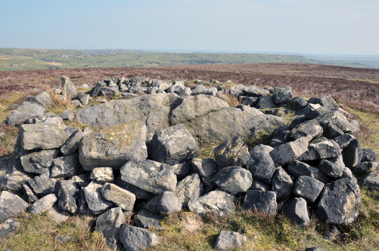 the exposed stones at the top of a cairn known as the millers grave on midgley moor in calderdale west yorkshire with surrounding pennine landscape and the calder valley in the distance