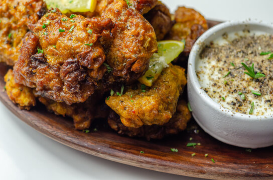 Delicious onion bhaji fritters served on wooden plate with white dip