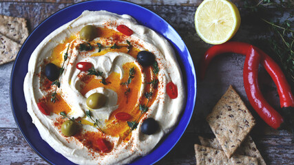 Hummus with olives, paprika and olive oil in a blue plate. A traditional Middle Eastern snack.