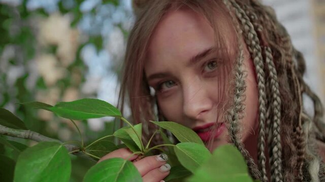 A cute girl with dreadlocks poses by a tree with leaves