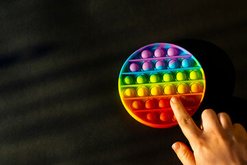 Trendy colorful anti-stress sensory toy. Silicone fidget push pop it for fine motoric skills lies in the sun. Flat lay on black background. Picture with place for text.
