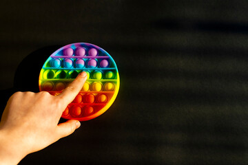 Trendy colorful anti-stress sensory toy. Silicone fidget push pop it for fine motoric skills lies in the sun. Flat lay on black background. Picture with place for text.