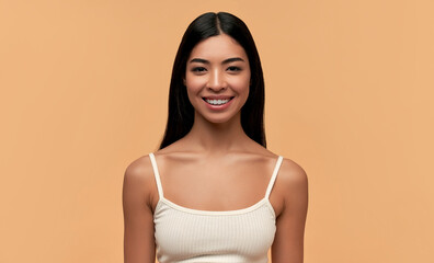Young Asian woman with clean healthy glowing skin in white top isolated on beige background. Facial...