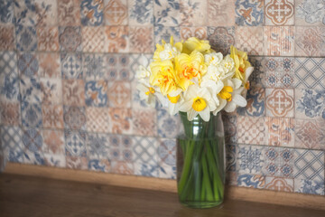 A bouquet of many daffodils in a glass vase on the kitchen table. Design concept.