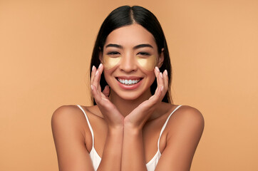 Young Asian woman in white lingerie and clean radiant skin with moisturizing patches under the eyes on a beige background. Spa care, cosmetology.