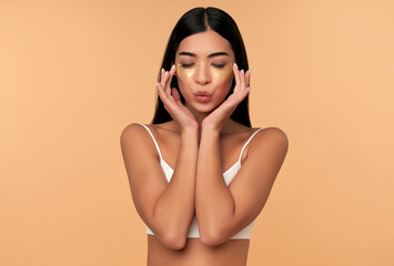 Young Asian woman in white lingerie and clean radiant skin with moisturizing patches under the eyes on a beige background. Spa care, cosmetology.