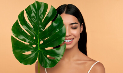 Young Asian woman in white lingerie and clean radiant skin with a green leaf on a beige background....