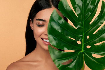 Young Asian woman with clean radiant face skin with green leaf on beige background. Spa care,...