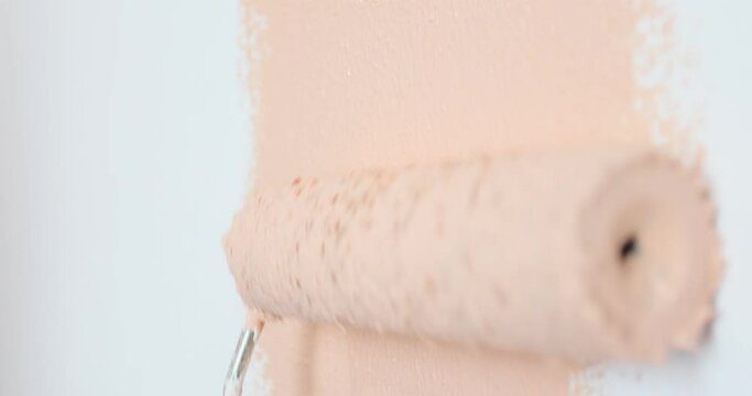 Closeup of painter man hand painting with a roller. Anonymous painter man at work painting a orange old wall with stains in need of a makeover and renovation. Professional painting services.