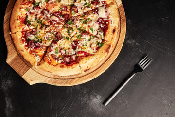 pizza on a wooden base on a black textured background top view