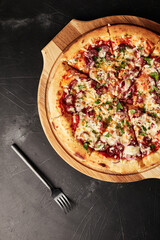 pizza on a wooden base on a black textured background top view