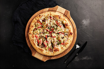 pizza on a wooden base on a black textured background top view