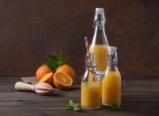 fresh orange juice in three bottles with citrus fruits on  a brown wooden background. Rustic concept. Front view