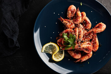 shrimp on a blue plate with lemon on a black textured background top view
