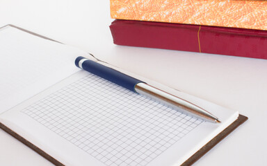 Stack of notebooks and open notepad with pen white background