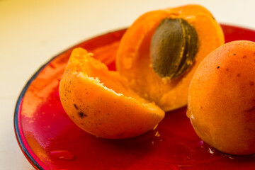 halves of a large fresh apricot on a red saucer, close-up