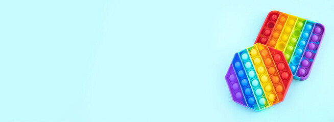 Colorful anti-stress fidget push pop it sensory toys isolated on blue background. Simple dimple. Top view, flat lay, copy space. Selective focus. Banner
