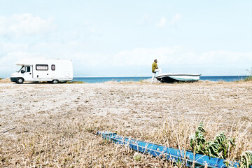 Man on the beach near the boat and white camper parked by the sea. Tourist season on the mediterranean sea. Sicily. Ionian Sea.