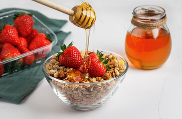 Muesli with strawberries and honey in a glass plate, isolated on a white background. A honey stick.