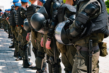A perspective photo of a row of armed special police workers with helmets in their hands. Ready to calm up the protest. Street. Crowd. Cruelty. Protective suits