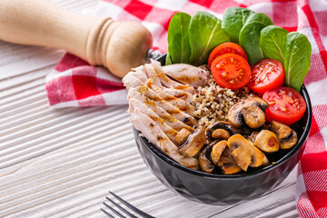 bowl of healthy quinoa with grilled chicken and vegetables on a white rustic wooden background