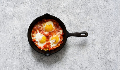 Shakshuka in a frying pan on the kitchen table. Dish of eggs, tomatoes and peppers, onions. Breakfast with vegetables and eggs..