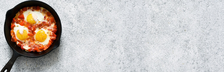 Shakshuka in a frying pan on the kitchen table. Dish of eggs, tomatoes and peppers, onions. Breakfast with vegetables and eggs..