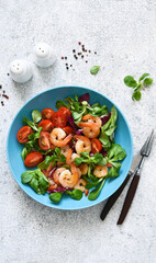 Mix salad with shrimps, tomatoes and leaves in a blue plate on the kitchen table. View from above.