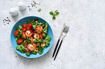 Mix salad with shrimps, tomatoes and leaves in a blue plate on the kitchen table. View from above.