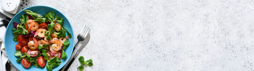 Mix salad with shrimps, tomatoes and leaves in a blue plate on the kitchen table. View from above.