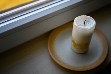 An extinguished large candle on a stone plate by the window.