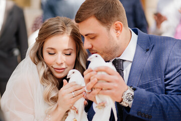 The bride and groom are holding a pair of white pigeons.