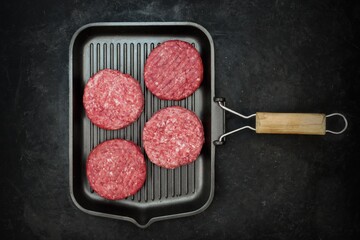 Raw Minced Homemade Grill Beef Burgers in Frying Pan, Top View. Griddle Grill Pap and Ground Beef Meat Patties for Grilling on Black Background, Overhead View. Raw Steak Burgers Cutlets On Grill Pan.