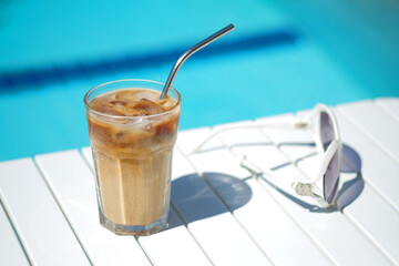 Ice coffee Cyprus Frappe Fredo against blue clear water of the swimming pool, on white table, with...