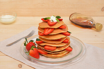 pancakes with strawberries and cream and maple syrup for them on the table