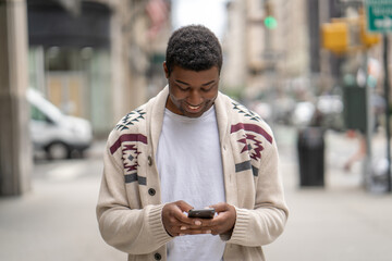 Naklejka premium Young black man in city walking street texting on cellphone