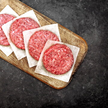 Homemade Beef Pork Burgers on Wooden Board, Top View. Raw Ground Beef Meat Steak Burgers Cutlets on Black Table Background, Overhead View. Farmers Uncooked Beef Burgers for BBQ Grilling Or Frying.